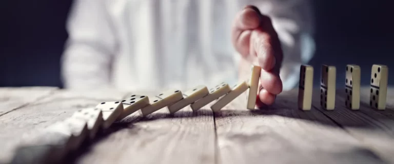 Hand stopt vallende dominostenen op houten tafel