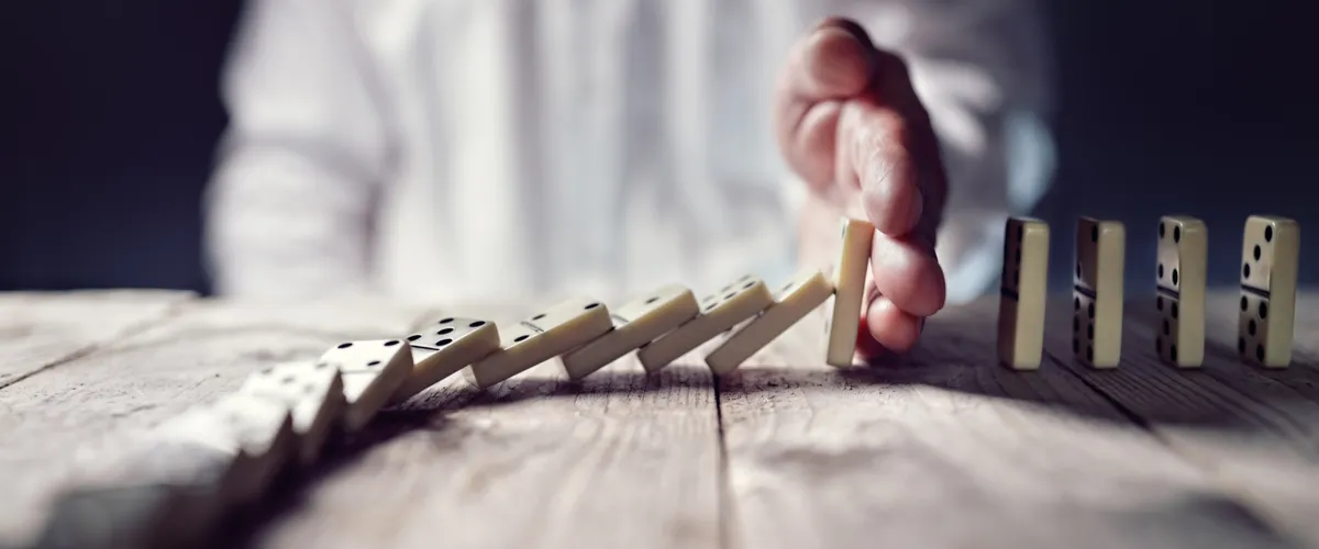 Hand stopt vallende dominostenen op houten tafel